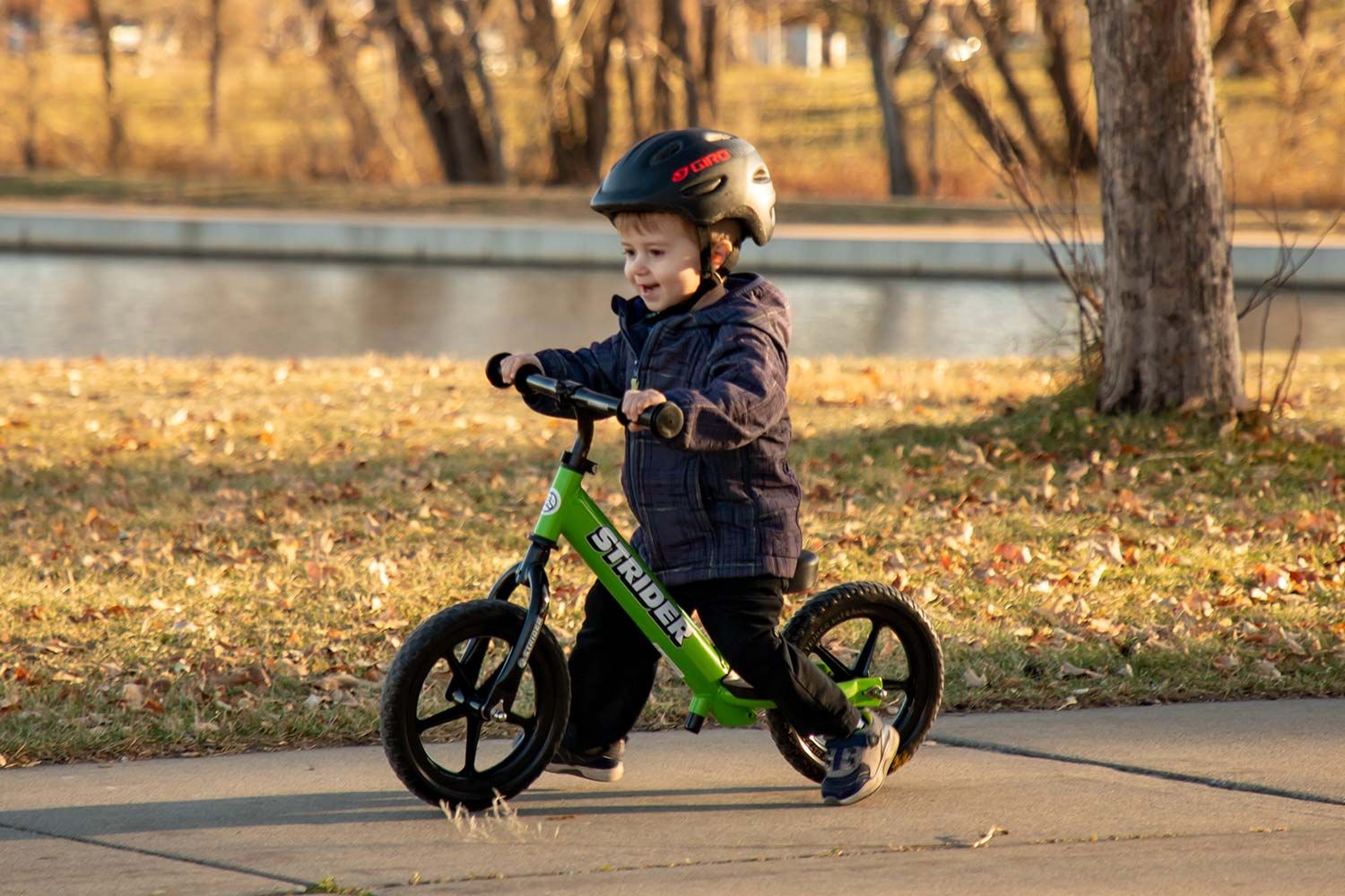 A boy on a green Strider 12 Sport balance bike with a Standard Stem and Aluminum Flat Handlebar