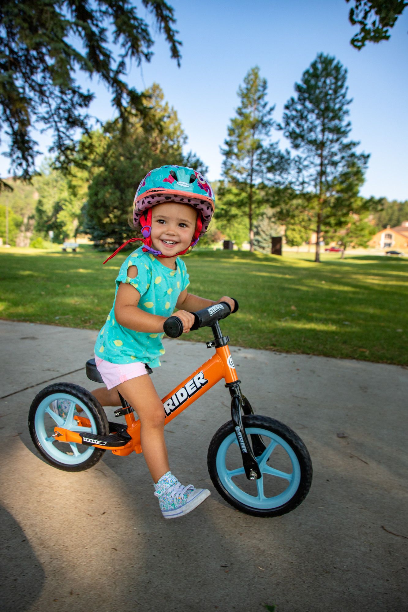Girl strides and smiles on an orange Strider 12" Sport balance bike